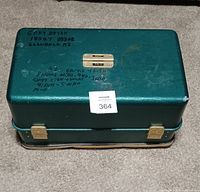 Closed green fishing tackle box with handwritten text on the lid and gold-tone latches, showing wear and missing handle.