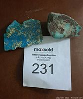 Photo showing two raw turquoise mineral specimens on a brown surface with auction tag 231