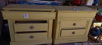 Pair of yellow wooden nightstands side by side, viewed from front with drawers closed and one drawer partially open