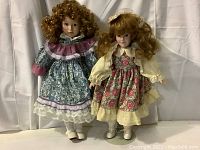 Two vintage porcelain dolls posed side by side, showing full front view