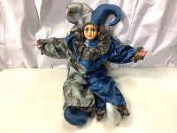 Front view of the Harlequin jester doll in sitting position on a white surface, showing full costume and musical box doll details.