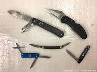 Five pocket knives and cutters arranged on a surface showing blades and handles.