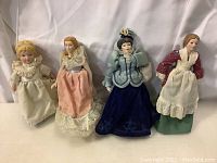 Four porcelain dolls standing side by side dressed in vintage attire