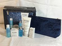 All items displayed with two cosmetic bags, showing contents of the Biotherm box set including skincare bottles and tubes