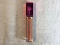 Front view of Lise Watier lip gloss in clear rectangular tube with dark pink cap showing product inside.