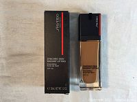 Photo of the Shiseido Synchro Skin Radiant Lifting Foundation bottle next to its box, showing packaging, branding, and shade details.