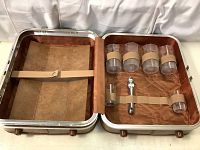 Open view of vintage portable cocktail case showing interior with four glasses secured by beige bands and bartender accessories inside a brown suede-lined case.