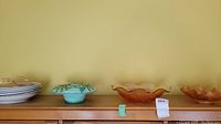 Collection of white ceramic plates, light blue ceramic bowl, and two large amber-colored glass bowls with leaf patterns on wooden shelf.