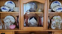 Wood cabinet shelves holding a collection of blue and white dishes, teapot, wine glasses, vases, and glassware items