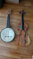 Photo showing the fiddle shaped clock and Stello 4-string banjo side by side on a wooden floor.