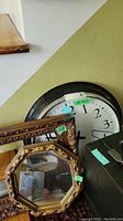 Wide photo showing large round black metal clock leaned against wall behind wood frames.