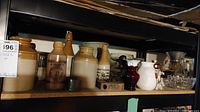 Overall shelf view showing assortment of stoneware crocks, bottles, jars, vases and glass bowls