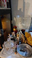 Photo showing clear cut glass jar, various figurines including children and performers, and a small metal dish with keys, set on a white surface