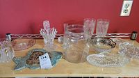 Display of glass and crystal items including ice bucket, glasses, ceramic fish dish, and various serving dishes on a wooden table against red background.