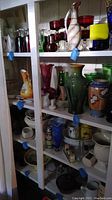 Shelf with multiple glassware items including vases, red drinking glasses, colorful bowls and decorative pieces