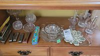 Overall lot of five harmonicas and multiple decorative glass items including a bowl, plater, baskets and snack dishes on a wooden shelf
