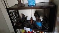 Wide view of six antique irons on shelf, showing various sizes, rust, and blue painted irons.