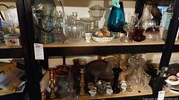 Full view of shelf containing glass jars, candlestick holders, glass vases, ceramic egg cups, and vintage crocks.