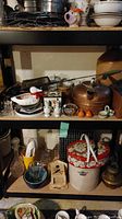 Shelving unit showing antique copper kettle, ceramic duck container, salt and pepper sets, jugs, crocks, oil lamp, and decorative tins.