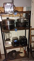 Shelf with three chrome two-slice toasters, glass blender with chrome base, enameled teapot, cast iron frying pan, stainless steel pots with lids, and metal strainer.