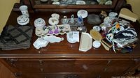 Wide photo of assorted ladies accessories displayed on wooden dresser including scarves, jewelry, bottles, dishes, brushes.