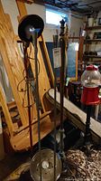 Three vintage floor lamps in basement setting, showing metal cover hanging lamp with bulb and exposed wiring, along with other lamps in the same group.
