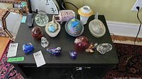 Overview of all vintage hen-on-nest dishes and artisan glass paperweights on black table.