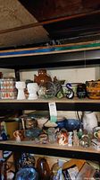Shelf view of collectable ceramic and glass items including cookie jar, planters, figurines, pitchers, and bowls.