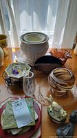 Overview showing ceramic planters, decorative bunny, various glass vases and bowls, carved duck figurines, and mixed stands on a tabletop with natural lighting.