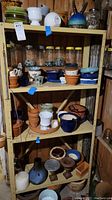 Four shelves showing various sizes, shapes, colors, and textures of planters and flower pots including terracotta, glazed ceramic, glass jars with marbles.