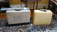 Two vintage portable sewing machines in their original cases sitting on a patterned rug in a room.