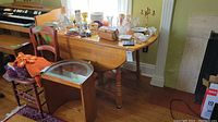 Rectangular solid maple drop-leaf table with multiple decorative items on top including glassware and ceramic figurines. Table has turned legs and drop sides partially extended.