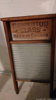 Wooden washboard with ribbed glass scrubbing surface and wood panel with printed text 'Competitor Glass Made in Canada'.