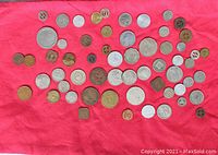 Photo of assorted coins and tokens laid out on a pink cloth showing variety of sizes and shapes.