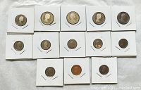 Fifteen Canadian coins displayed in individual white holders arranged on a surface. Coins vary in size and design, some possibly silver.