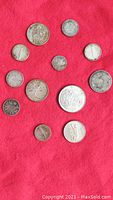 Twelve Canadian silver coins laid out on a red fabric background showing obverse and reverse sides.