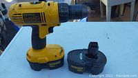Yellow DeWalt cordless drill with black ergonomic handle and attached 18V battery beside a second detached 18V battery on a white surface.