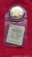 100 Korona Hungarian gold coin in protective capsule placed above a certificate of authenticity on red cloth.