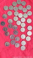 Photo of 48 Canadian quarters from 1973 featuring centennial designs laid out on red cloth.