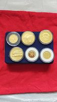 Set of six gold plated US tribute coins displayed in blue holder on red cloth background, showing obverse and reverse sides.