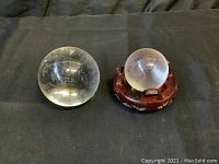 Two clear crystal balls placed on a black fabric background; one larger and one smaller on a wooden stand.