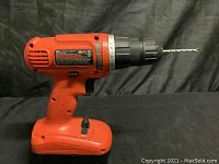 Side view of red Black & Decker cordless drill with drill bit inserted in chuck, resting on black cloth background.