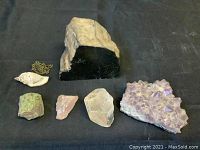 Full lot overview showing all stones, crystals, seashell pendant and chain on black fabric background.