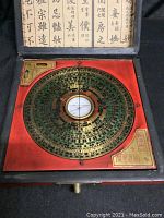 Top-down photo showing the large circular brass compass dial inside the red wooden box with intricate Chinese characters and markings on the dial.