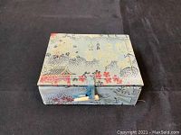 Closed fabric-covered box with floral and landscape pattern in muted colors, featuring a blue cloth and button clasp.