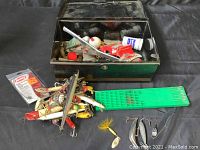 Fishing tackle box open with assorted fishing lures, hooks, and tools displayed outside the box