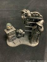 Front angle showing figurine with robed person, bookshelf, rabbit, chest of drawers, and books on base.