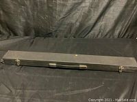 Closed black carrying case for pool cue with metal latches and handle, showing wear and some damage.