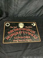 Front side of Quija board showing moon, sun, alphabet letters, numbers, Yes/No and Good Bye text with planchette in center.