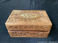 Angle view of rustic wooden jewelry box showing hand carved floral and leaf pattern with inlaid leaf motif on top.